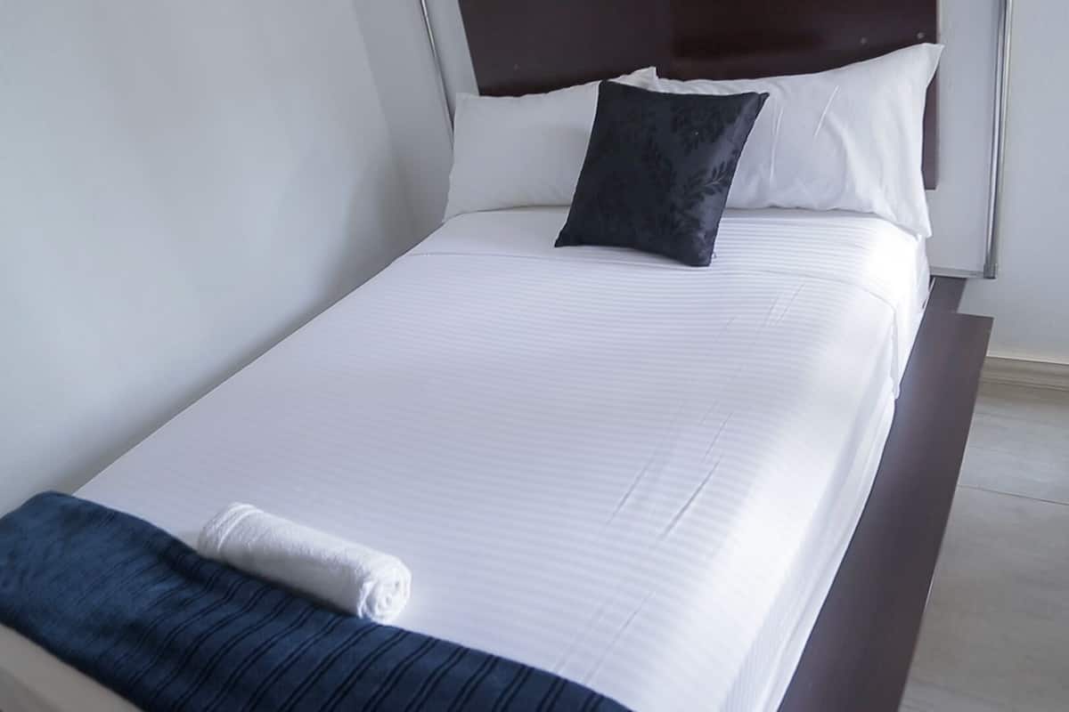 A neatly made bed with white linens and a dark blue throw blanket, a pillow, and a folded towel on the side.