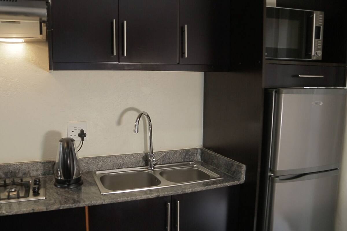 A modern kitchen with a gas stove, a kettle, a double sink, and stainless steel appliances.