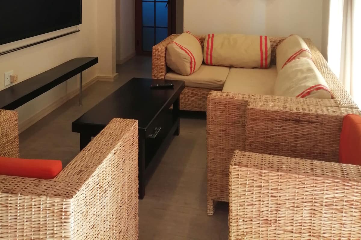 A living room with a flat-screen TV, a sofa, two wicker chairs, a coffee table, and a wall-mounted decorative piece.