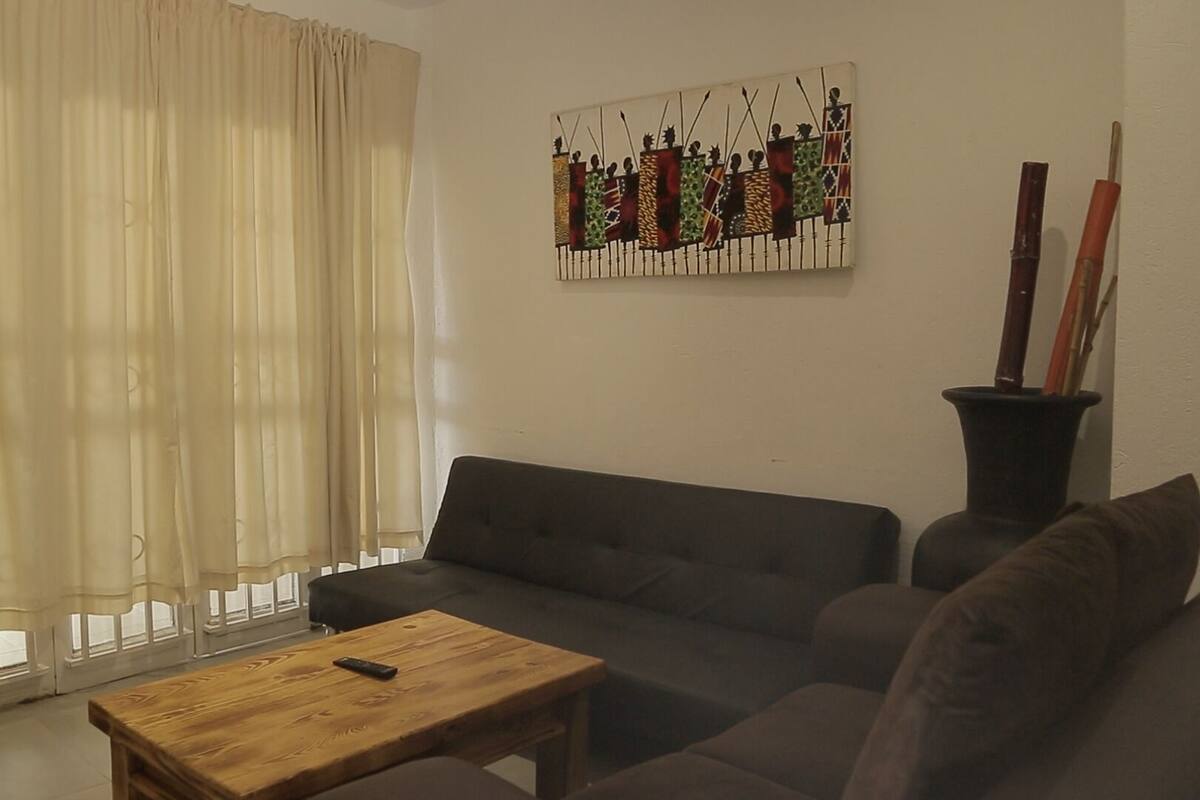A living room with a sofa, a coffee table, a painting on the wall, and a window with curtains.