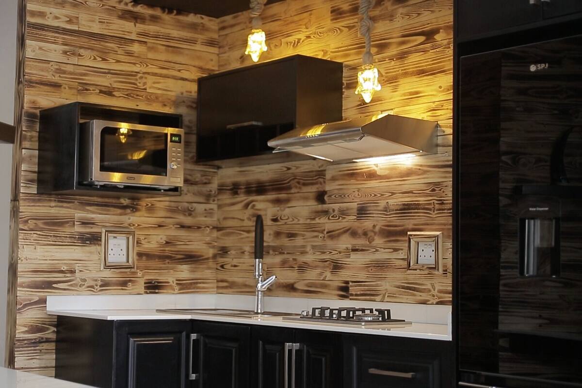 A modern kitchen with wooden paneling, a stainless steel microwave, a gas stove, and a built-in oven.