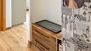 Una habitación con piso de madera, un mueble pequeño de madera con cajones, un tendedero metálico e ilustraciones de estilo vintage en la pared.