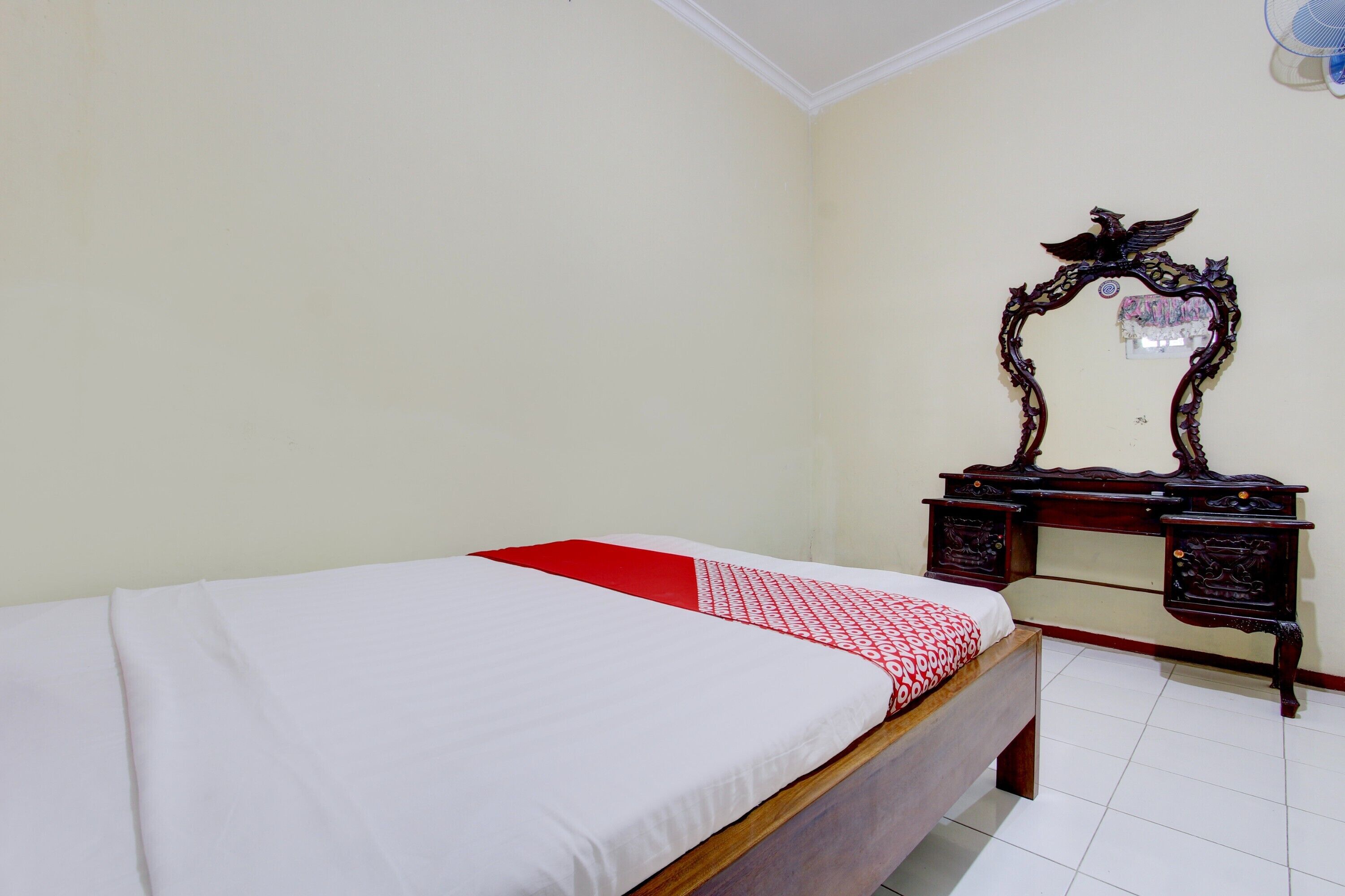 A bedroom with a single bed, a wooden desk with a mirror, and a red and white patterned bedspread.