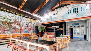 An indoor seating area with wooden benches and tables, a mural on the wall, and a building entrance with signage. - Hotel O Homestay Joglo Dephis Syariah (Borobudur)