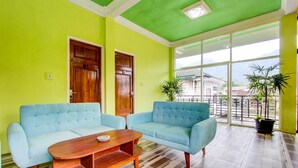 A bright room with two light blue sofas, a wooden coffee table, and a large window offering a view of buildings and mountains. - Hotel O Homestay Joglo Dephis Syariah (Borobudur)