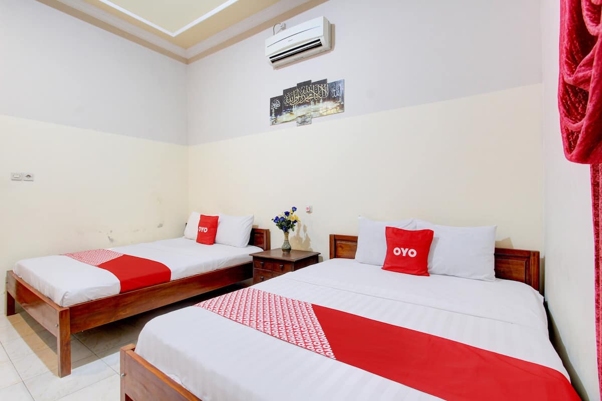 Habitación de hotel con dos camas, cada una con ropa de cama roja y blanca, una mesita con un jarrón de flores y un aire acondicionado de pared.