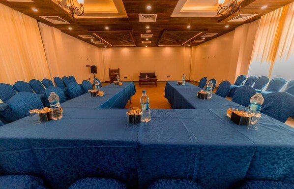 Une salle de conférence dotée de chaises et de tables recouvertes d’un tissu bleu, ainsi que de bouteilles d’eau et de verres.