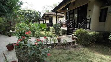 A traditional building with a porch and steps, surrounded by a garden with various plants and flowers.