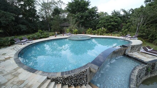 A circular swimming pool with a stone deck and lounge chairs around it. - Banbas Resort, Chitwan (Sauraha)