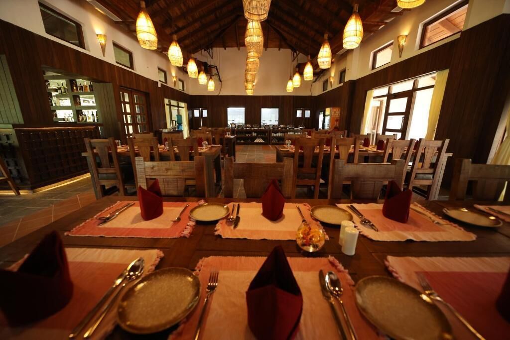 A restaurant with wooden tables set for dining, a bar area in the background, and warm lighting.