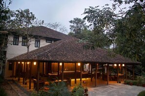 A covered outdoor seating area with tables and chairs, surrounded by potted plants and trees. - Banbas Resort, Chitwan (Sauraha)