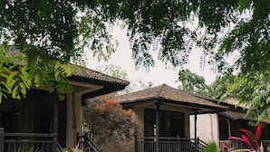 A traditional house with a tiled roof, a porch with a railing, and a stone pathway leading to the entrance. - Banbas Resort, Chitwan (Sauraha)