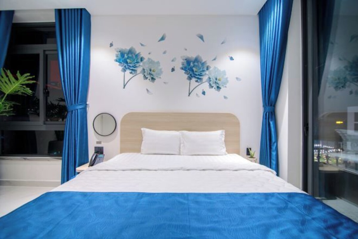 A modern bedroom with a large bed, blue curtains, and a wall with blue floral artwork.