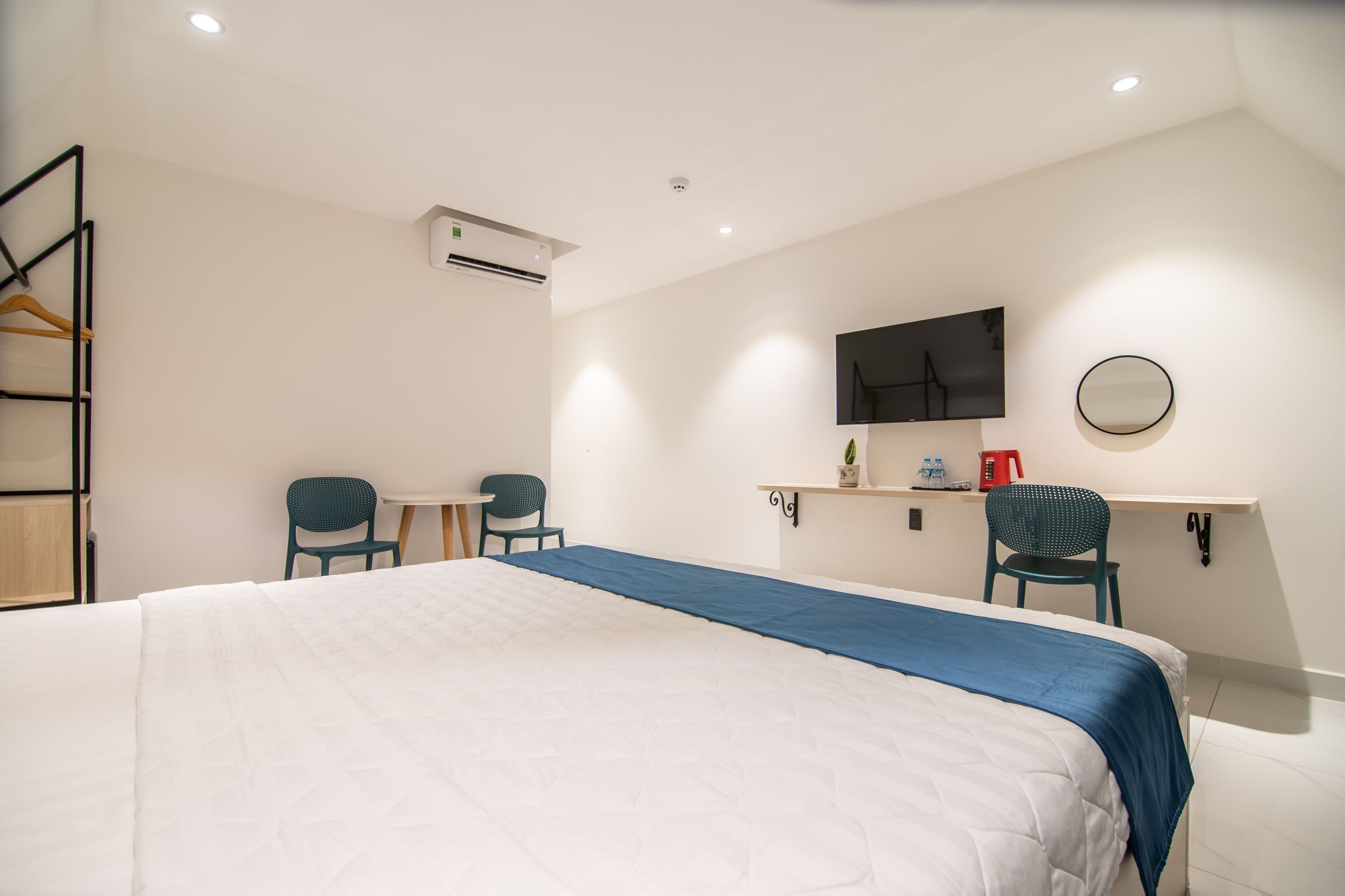 Ein Hotelzimmer mit einem großen Bett, zwei Stühlen, einem kleinen Tisch, einem Fernseher, einem Spiegel und einem Ablagefach mit Pflegeprodukten.