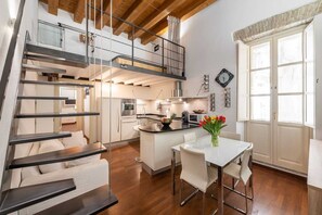 A modern kitchen with a central island, a dining area with a white table and chairs, and a staircase leading to a loft bedroom. - Appartamento (Cagliari)