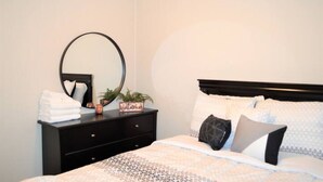 A neatly made bed with a patterned bedspread, a round mirror on a dresser, and a small plant on the dresser.