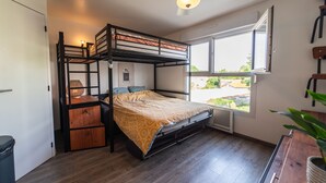 Quarto com beliche, janela, ventilador de teto e escrivaninha de madeira.