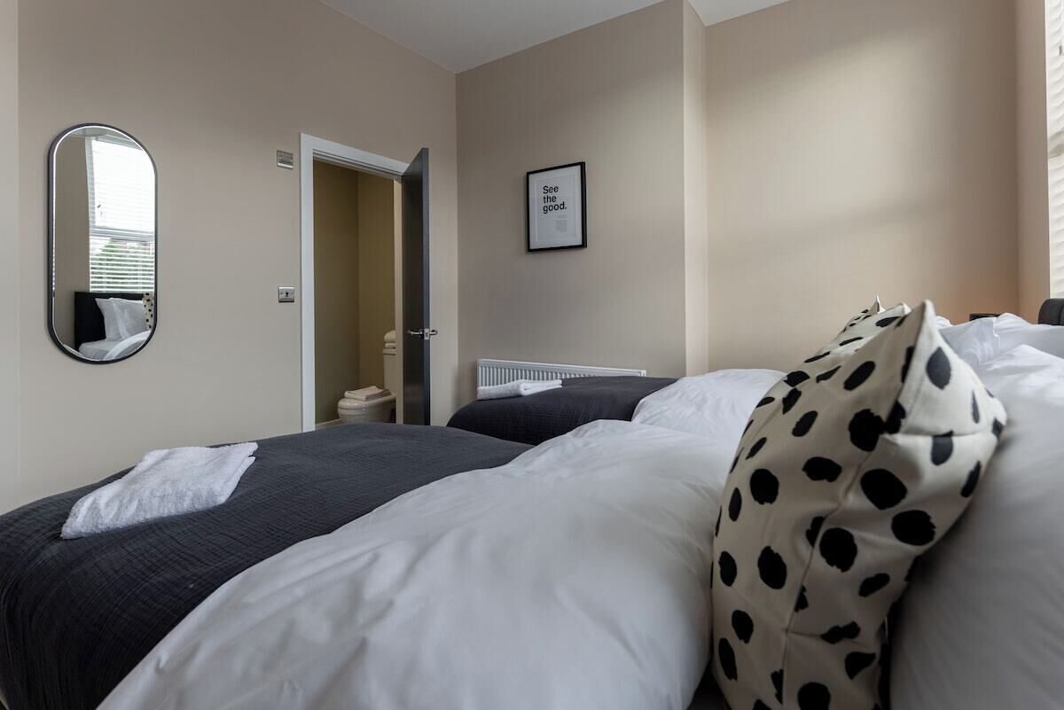 A hotel room with a bed, a mirror, a door leading to a bathroom, and a framed inspirational quote on the wall.
