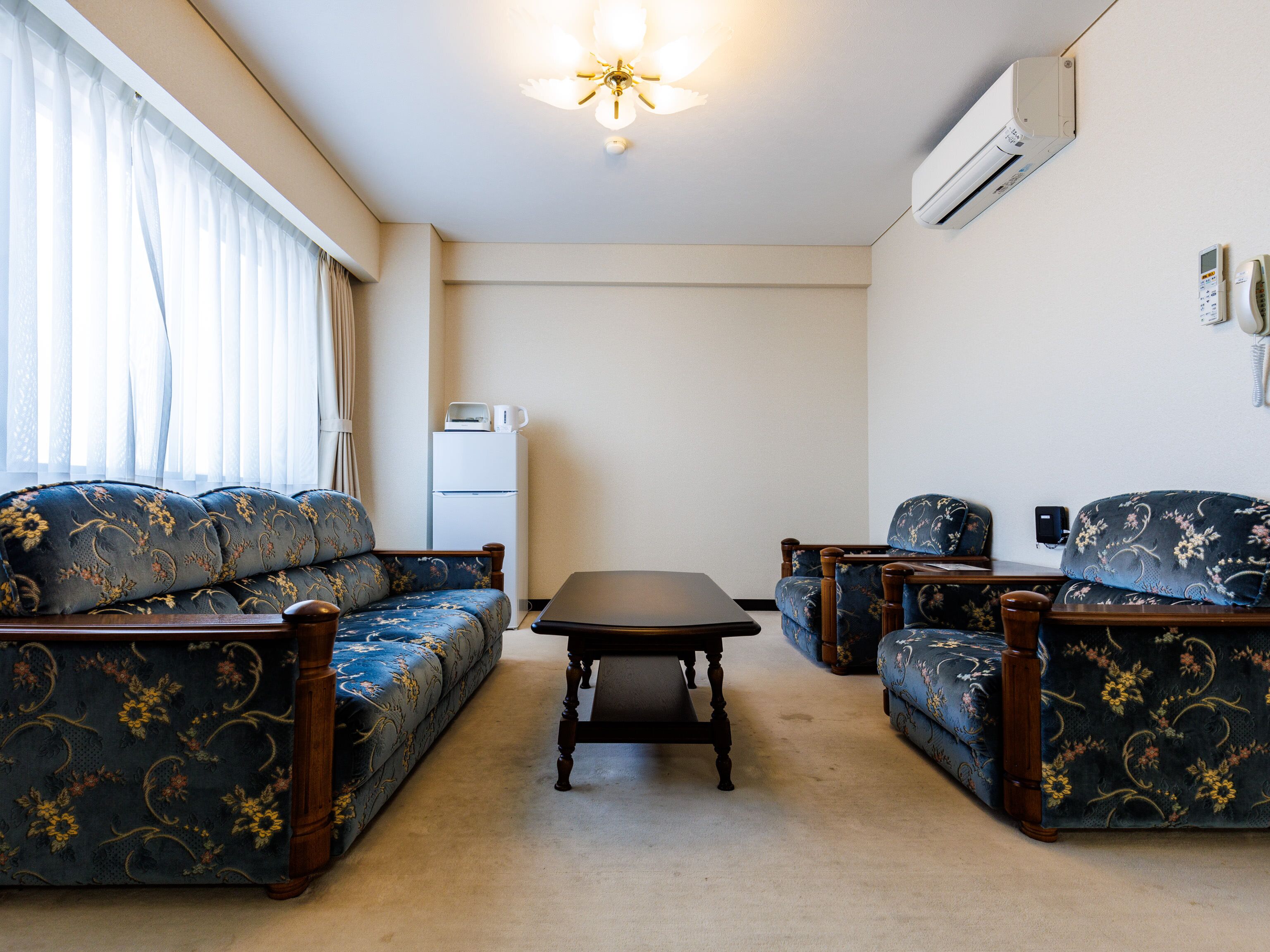 Una sala de estar con sofá, sillones, una mesa de centro y un refrigerador.
