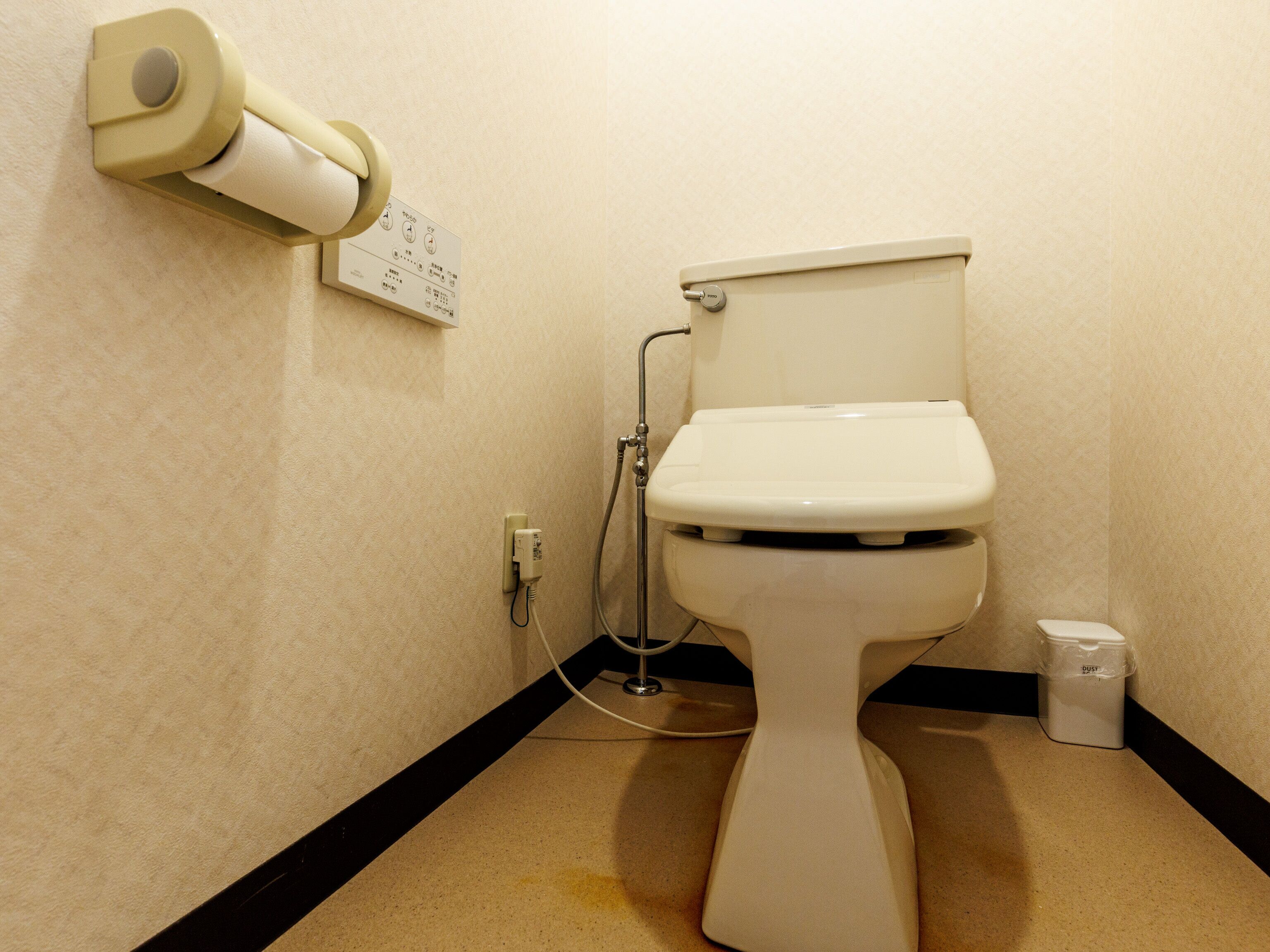 Eine Toilette mit Papierhandtuchspender, Handbidetschale und Mülleimer.