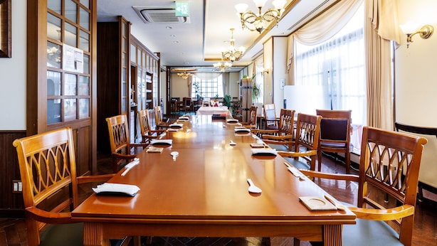 A long dining table with chairs, a chandelier, and large windows with curtains. - Tabist Hotel Nemuro Kaiyoutei (Nemuro)