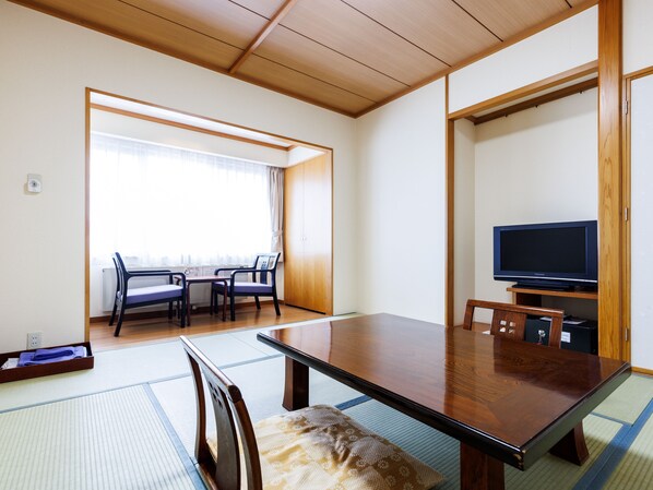Una habitación japonesa tradicional con suelo de tatami, una mesa de madera baja y un televisor sobre un atril de madera.