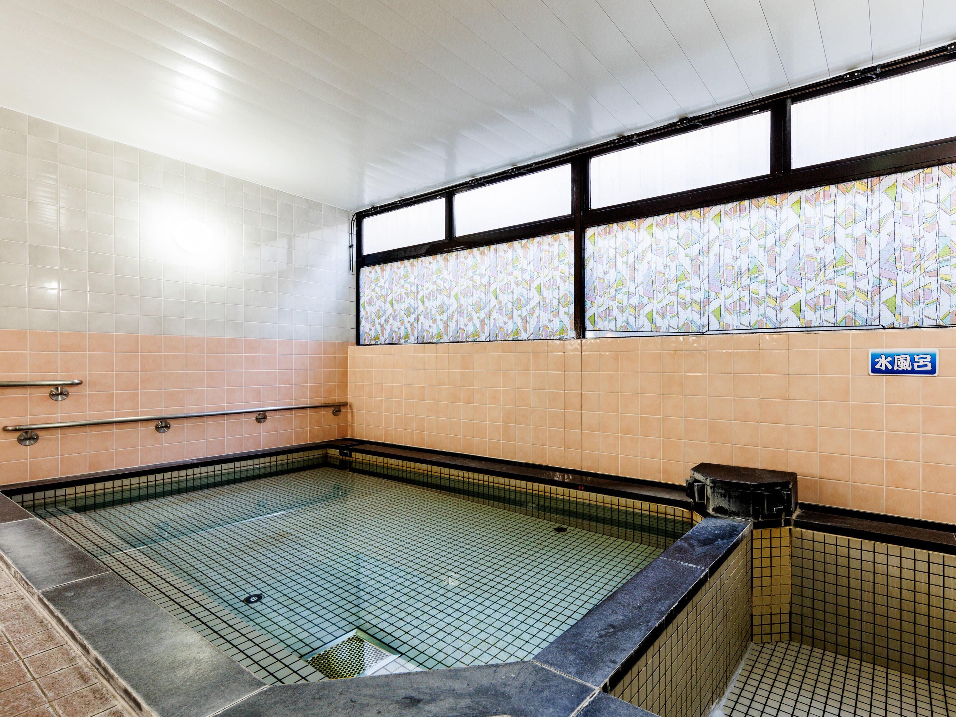 A tiled swimming pool with a tiled wall and a window with a colorful pattern.