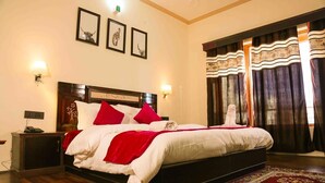 Una cama bien tendida con ropa de cama roja y blanca, un cabecero de madera y un tapete estampado en el suelo.