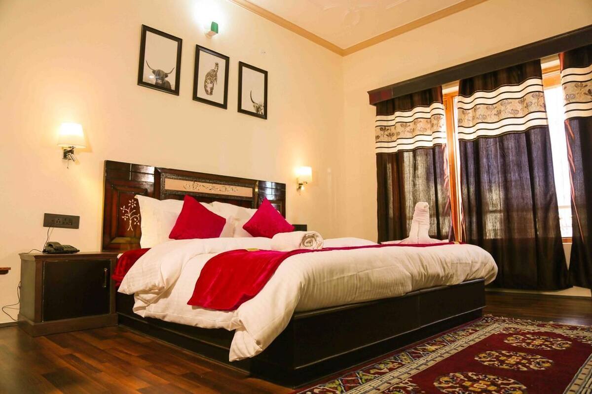 Una cama bien tendida con ropa de cama roja y blanca, un cabecero de madera y un tapete estampado en el suelo.