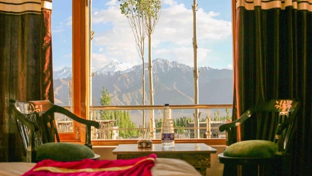 Una habitación con una cama, una mesa y una botella de agua, y vistas a las montañas a través de una ventana.
