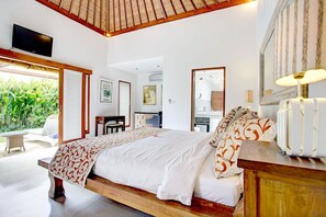 A spacious bedroom with a large bed, a wooden headboard, a bedside table, a mirror, and a TV mounted on the wall. - Sitara Villas Seminyak (Seminyak)