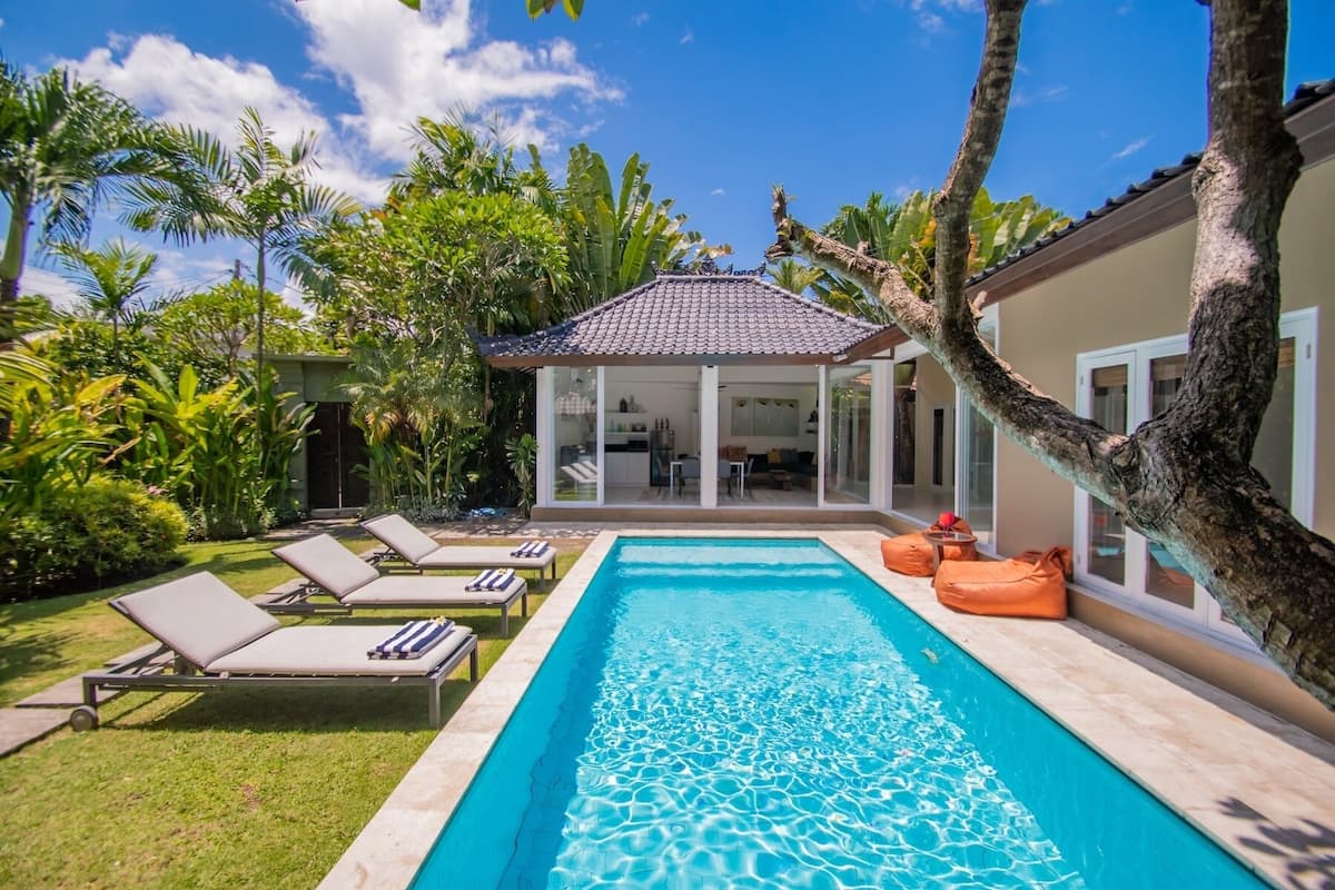 A swimming pool with lounge chairs, a covered patio, and lush greenery.