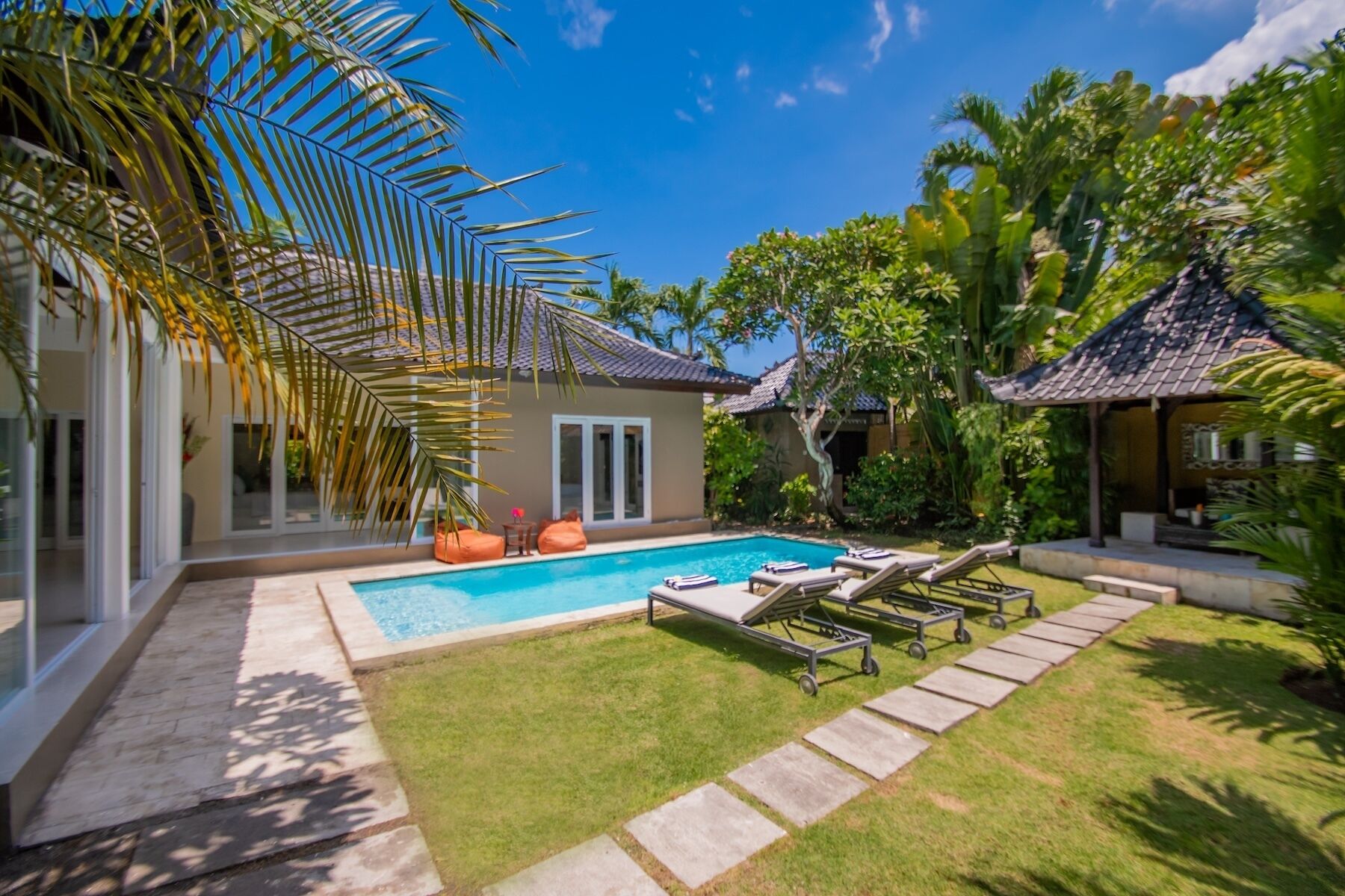Zona junto a la piscina con sillones de descanso, una piscina y abundante vegetación.