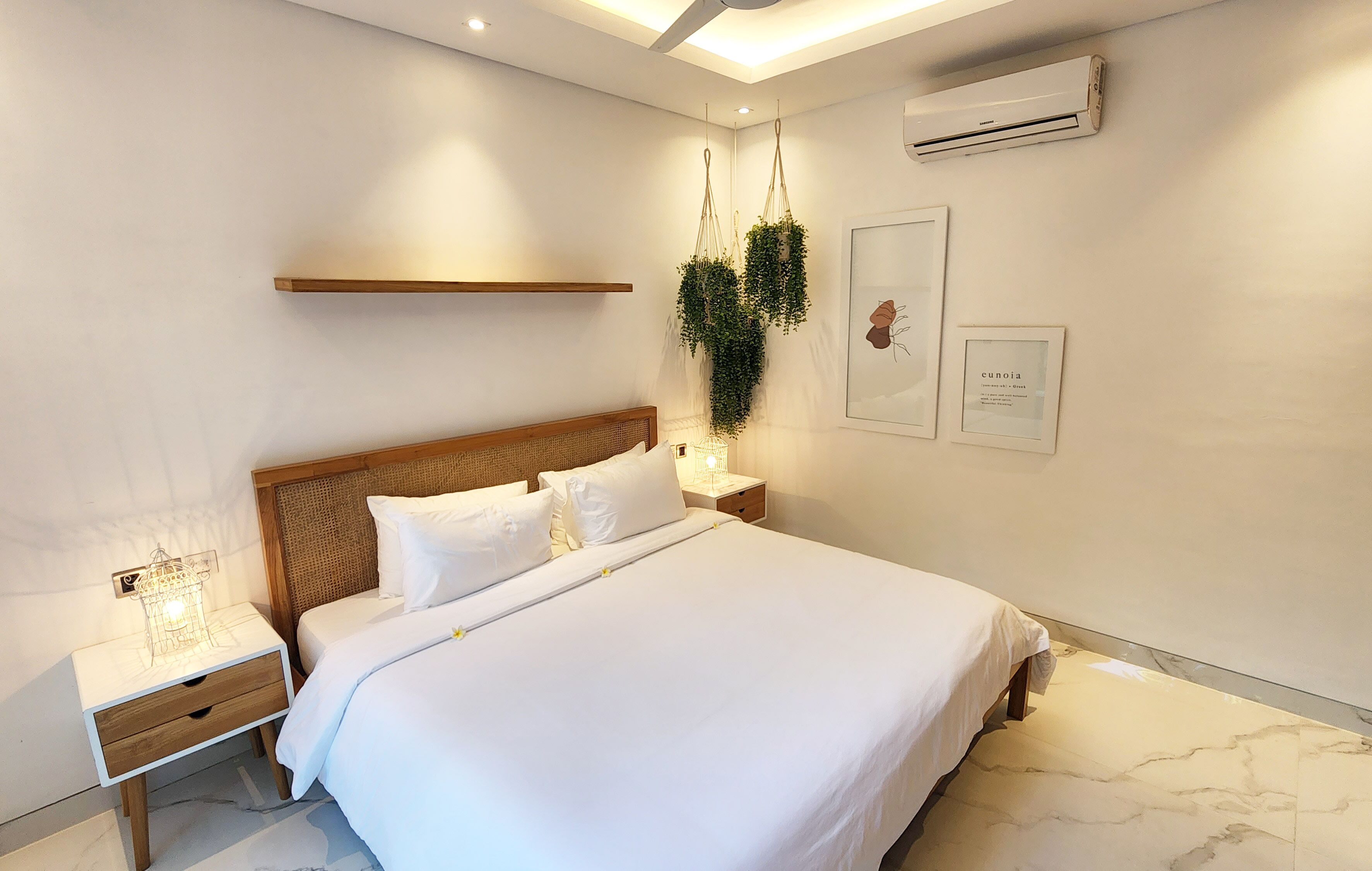 Una habitación de hotel moderna con una cama grande, cabecera de madera, mesitas de noche y plantas colgantes.