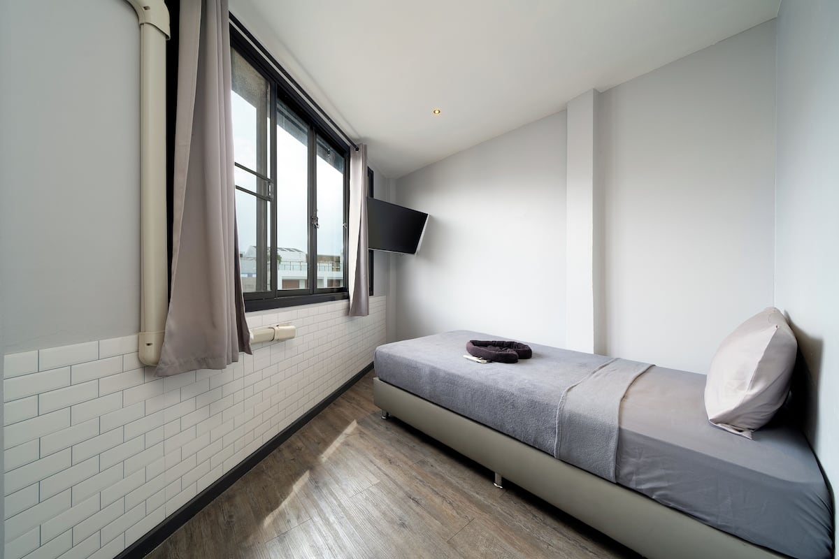 A small, modern room with a bed, a mounted TV, and a window with curtains.
