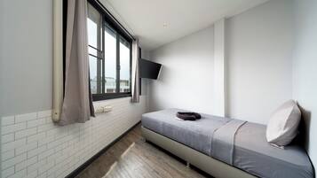 A small, modern room with a bed, a mounted TV, and a window with curtains.