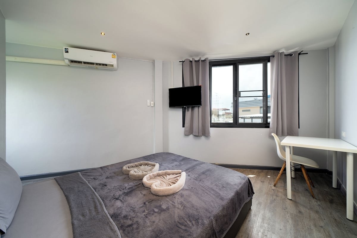 A modern hotel room with a bed, a desk, a TV, and a window with curtains.