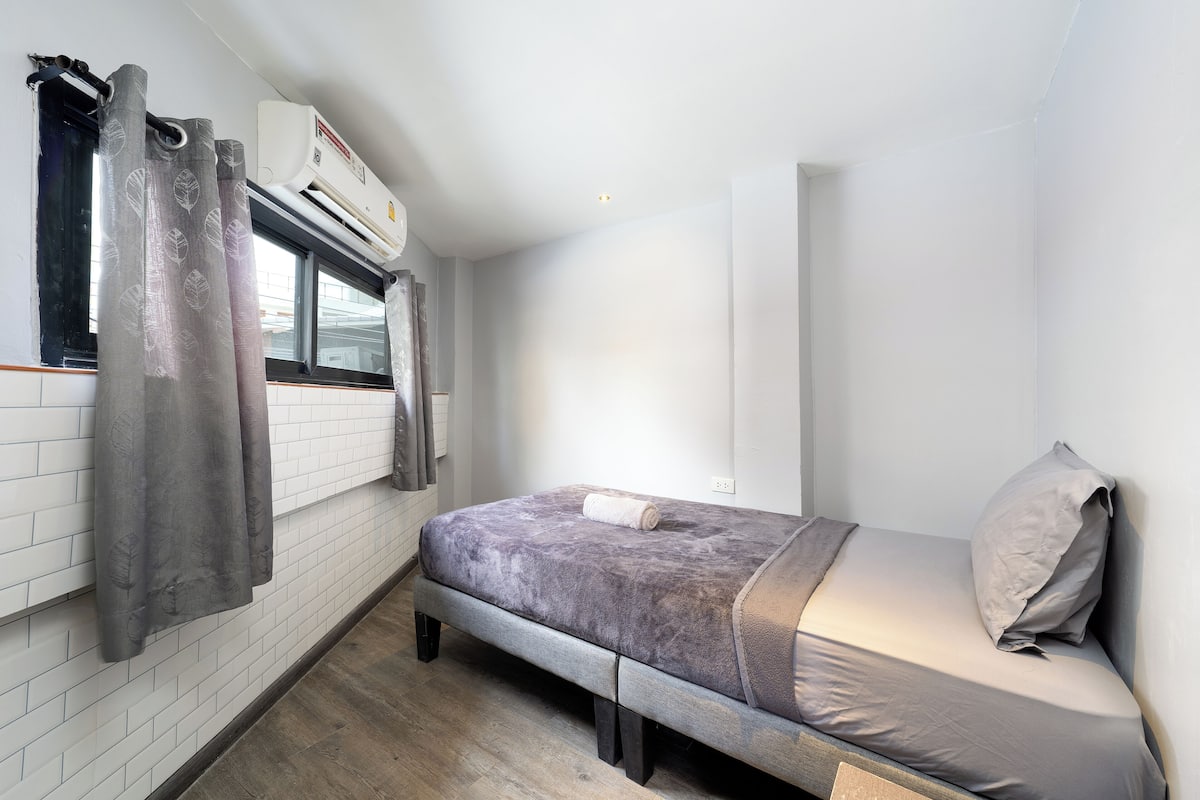 A compact room with a bed, a window with curtains, and an air conditioning unit.