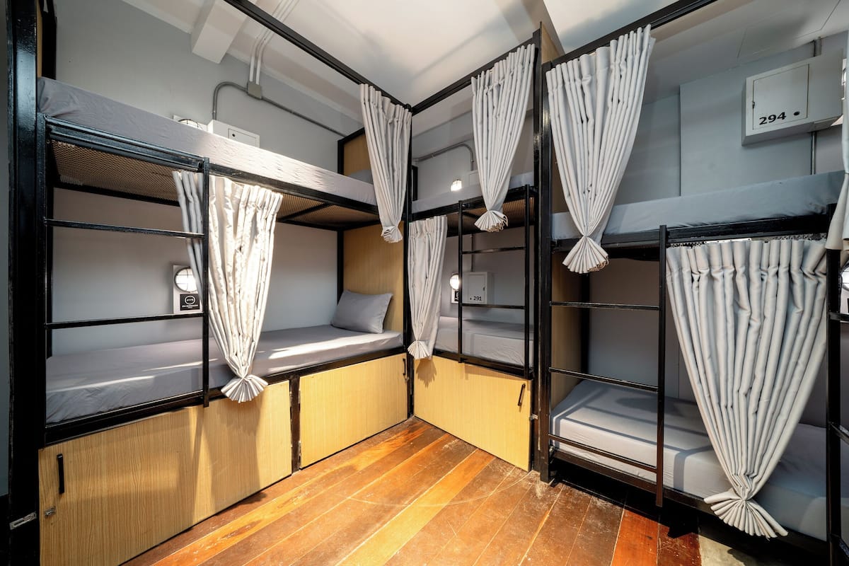 A dormitory-style room with bunk beds, wooden flooring, and curtains.