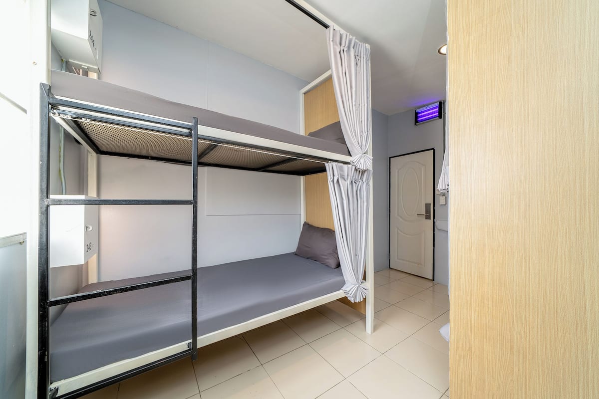 A bunk bed with a privacy curtain, a wooden door, and a small LED light.