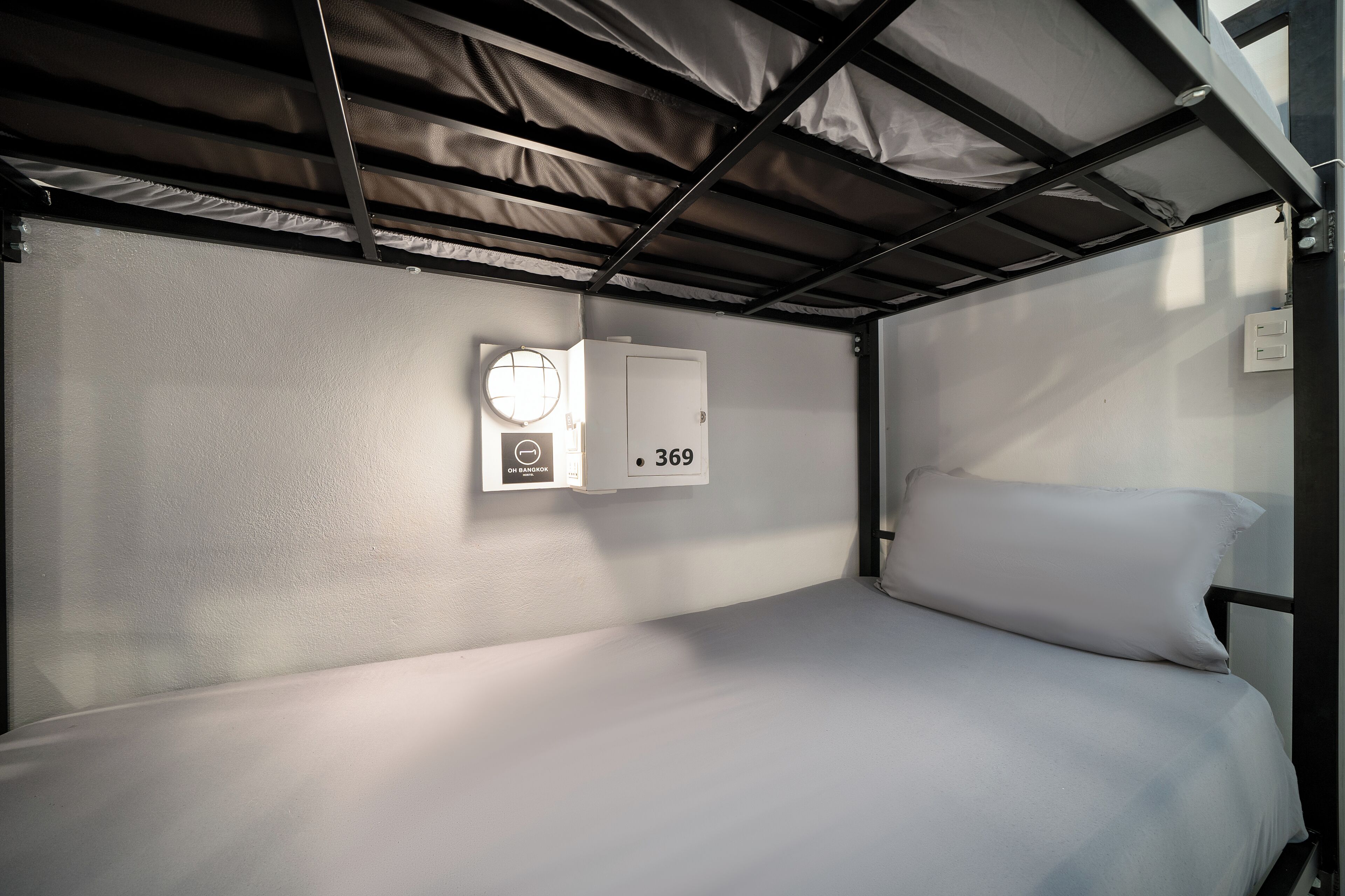 A bunk bed with a white mattress and pillow, a wall-mounted light fixture, and a thermostat.