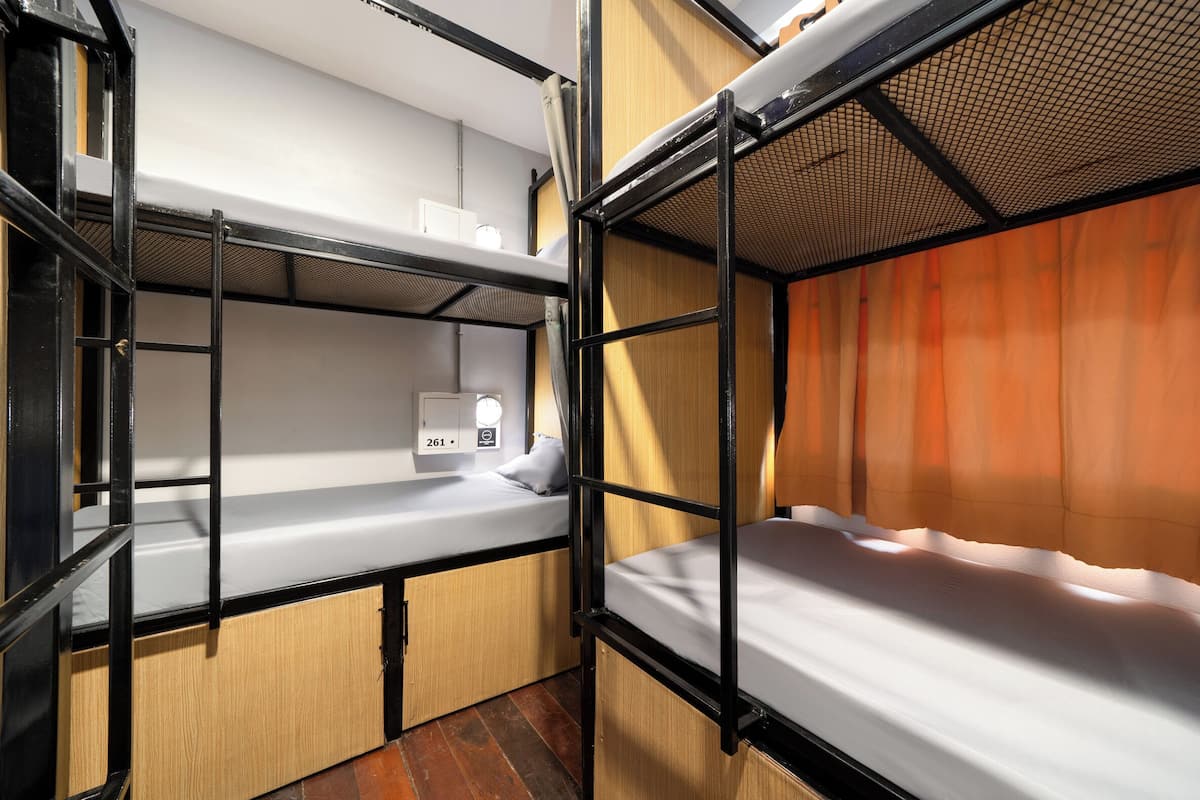 A bunk bed room with a white mattress, a small cabinet with a light, and a curtain.