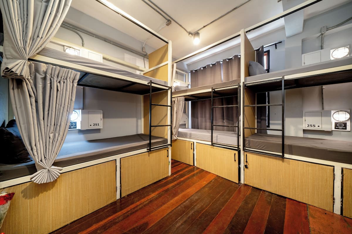 A compact room with bunk beds, wooden flooring, and a curtain on the left side.