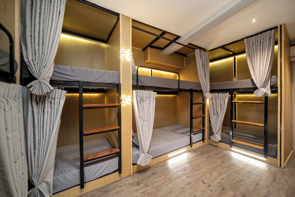 A bunk room with wooden bunk beds, curtains, and a number '53' on the wall.