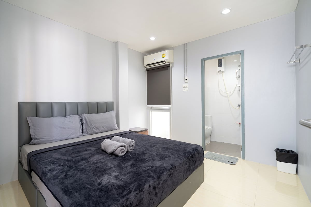 A modern bedroom with a large bed, a grey headboard, and a built-in air conditioning unit.