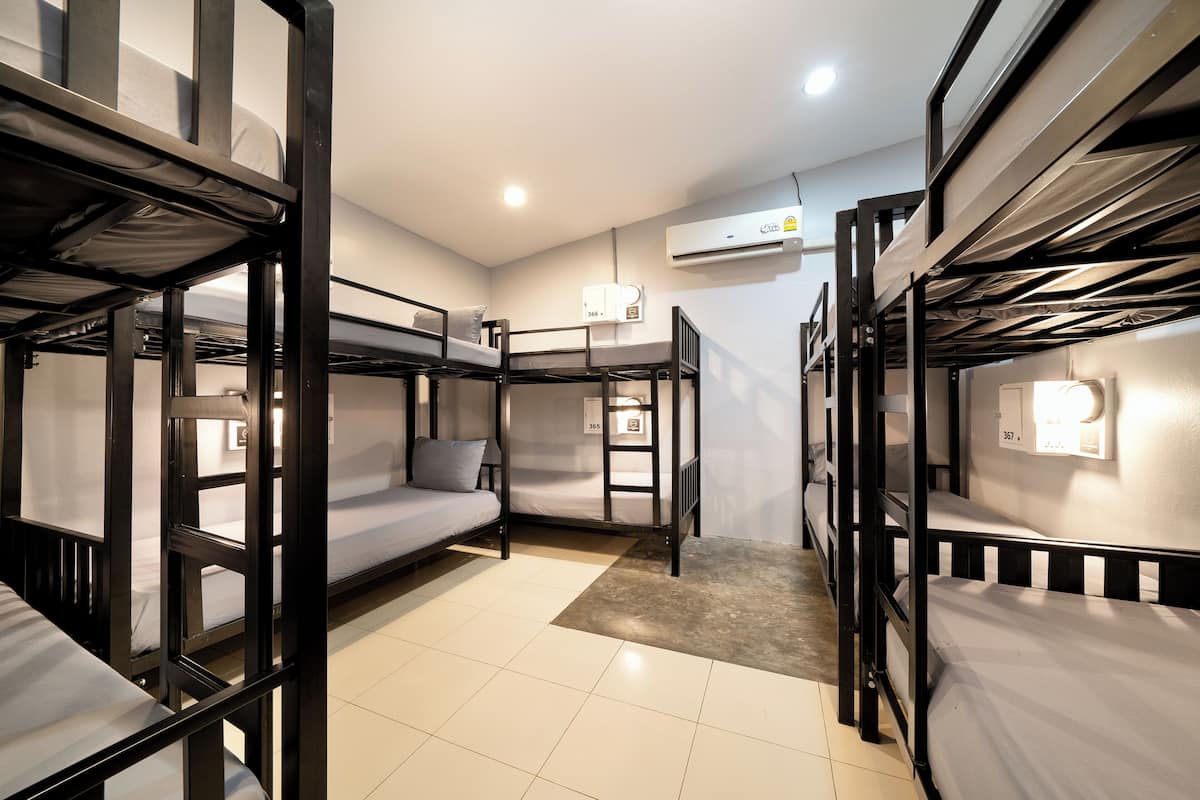 A dormitory room with bunk beds, an air conditioning unit, and a small rug.