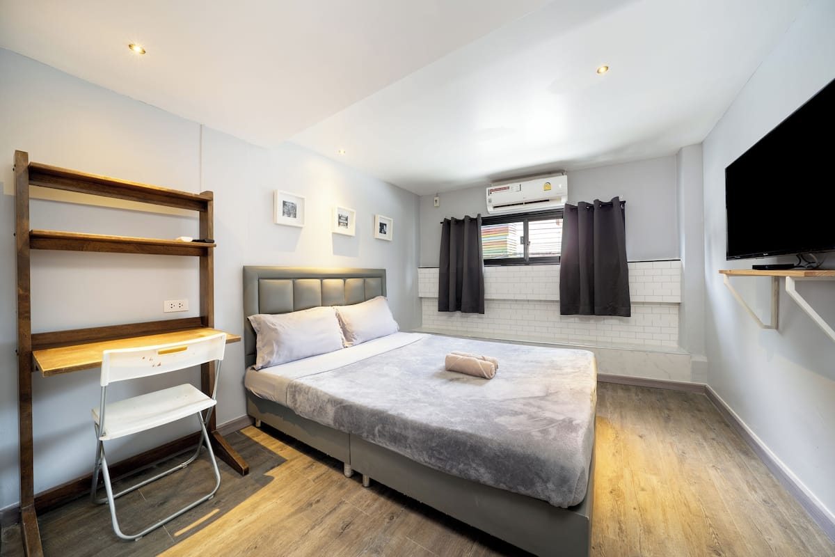 A modern bedroom with a bed, a desk, and a TV.