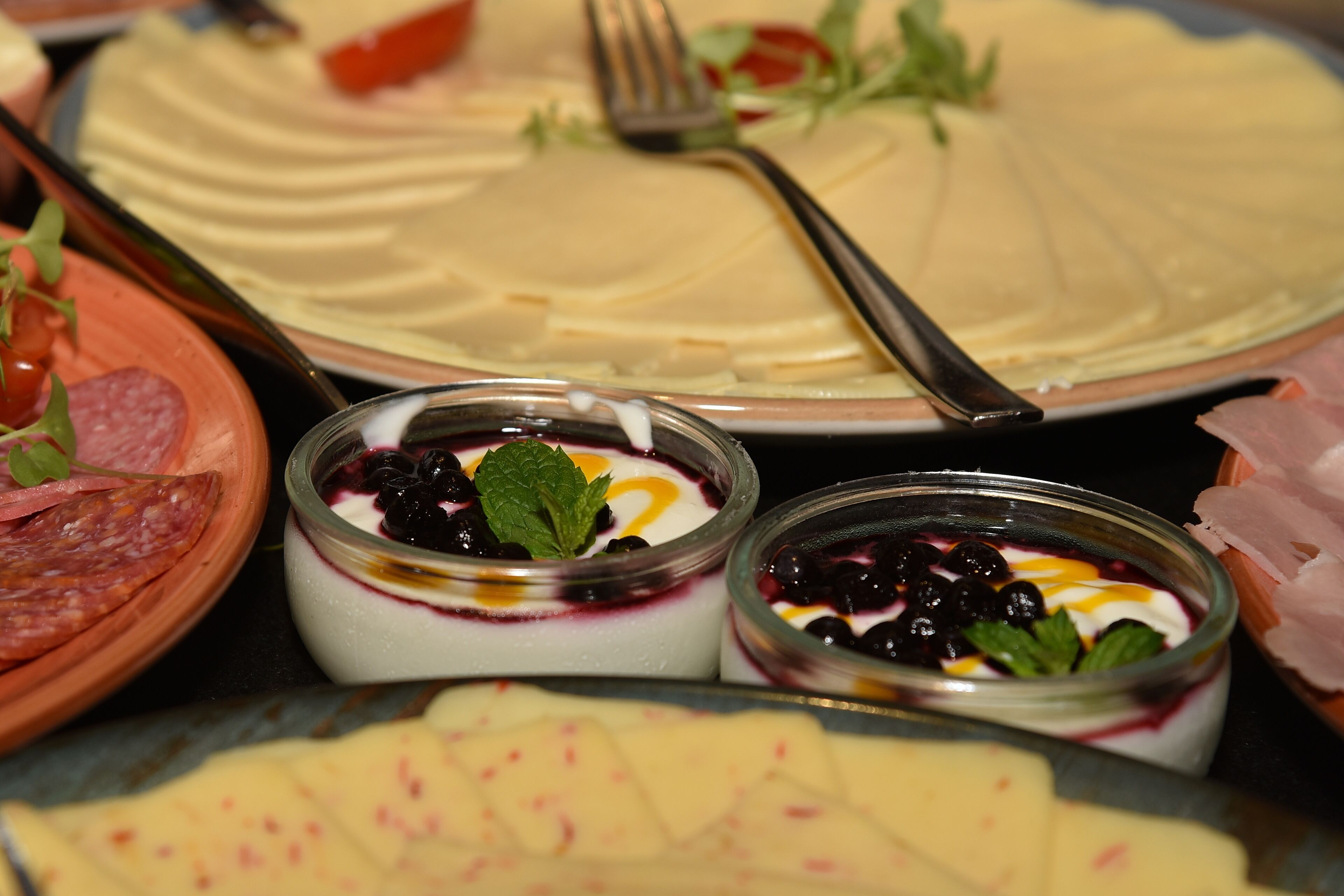 A variety of food items including a cake, cheese, and two small bowls with a creamy dessert and berries.