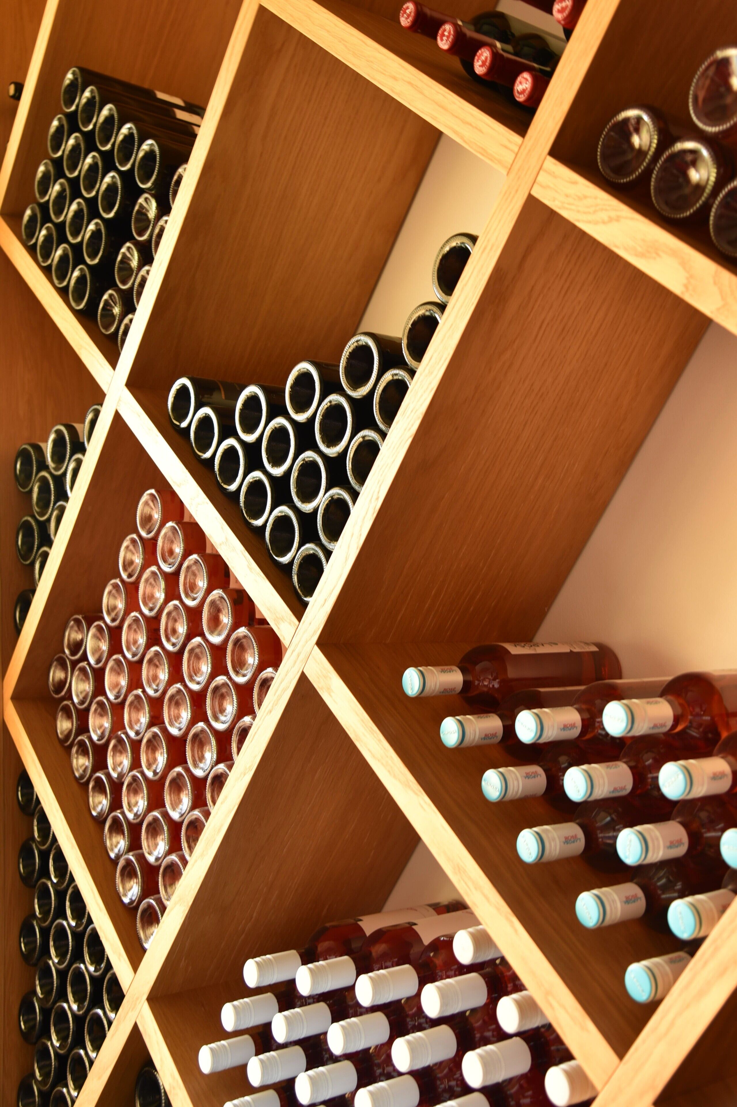 A wine rack with multiple rows of bottles and empty wine glasses.