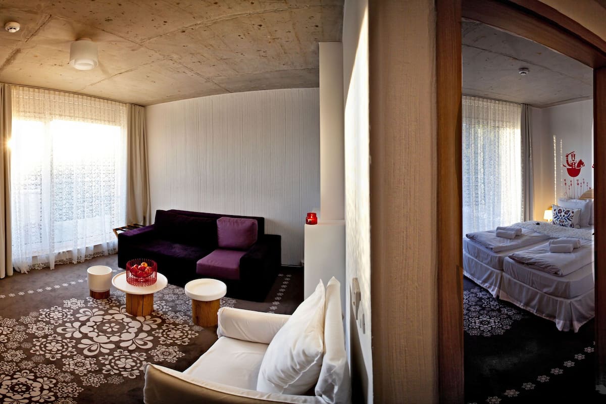 A hotel room with a bed, a sofa, a TV, and a small table with a basket.